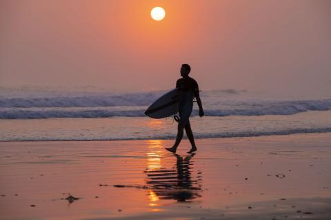 Surfer on beach at sunrise